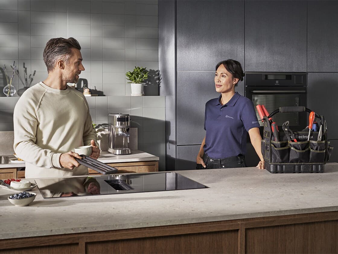 A man and a woman are standing at a kitchen sink. They are looking at an Electrolux product.