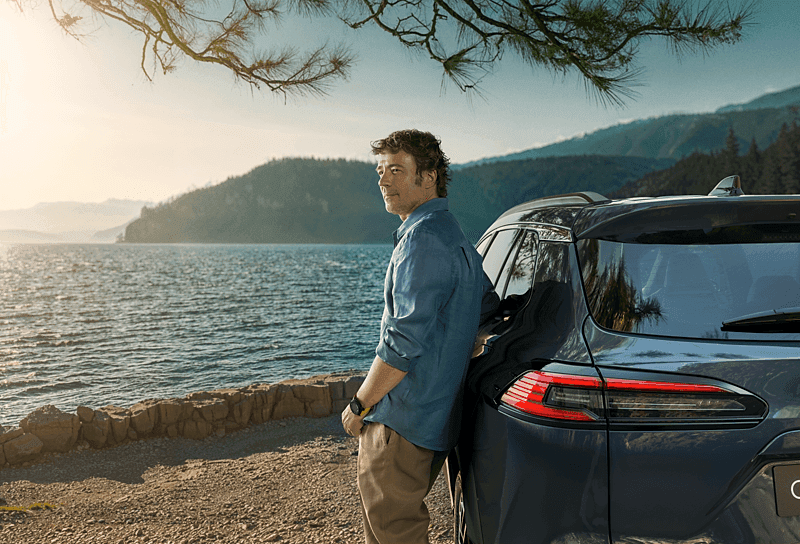 Man lutandes mot en Toyota bil med utsikt över havet och bergen.